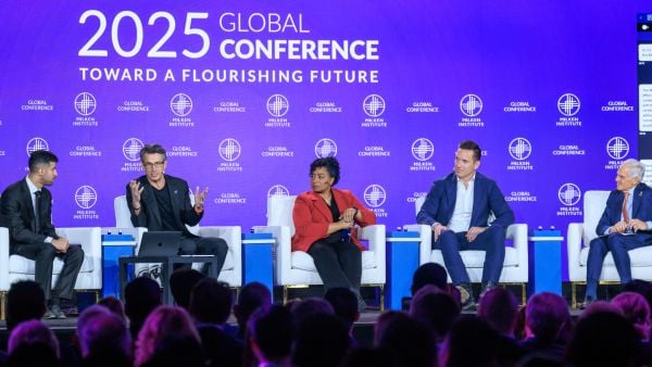 Panel of five speakers seated on stage at the 2025 Milken Institute Global Conference, with a vibrant purple backdrop displaying the event theme 'Toward a Flourishing Future,' as audience members watch.