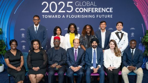 A group of men and women in business attire pose for a formal photo in front of a backdrop reading “2025 Global Conference – Toward a Flourishing Future.”