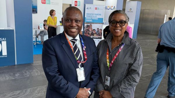 Two people smiling at a conference, wearing badges with booths in the background.