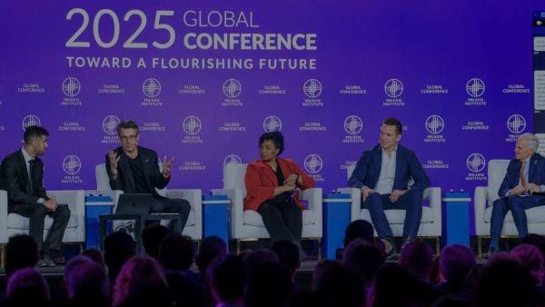 Panelists speak on stage at the 2025 Milken Institute Global Conference, with a backdrop reading “Toward a Flourishing Future” and an audience in the foreground.