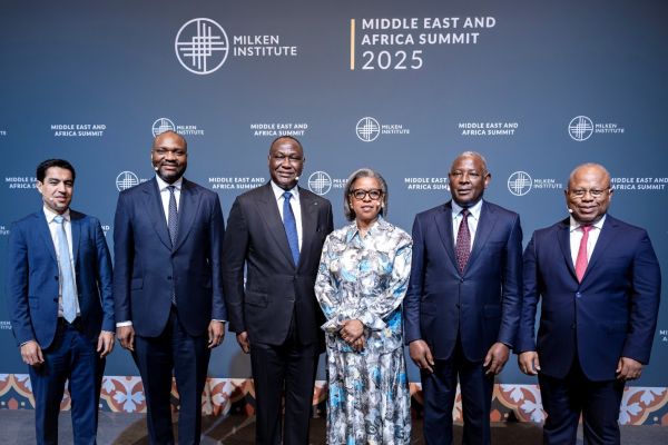 Six professionals, five men in suits and one woman in a patterned dress, pose for a group photo in front of a Milken Institute Middle East and Africa Summit 2025 backdrop.