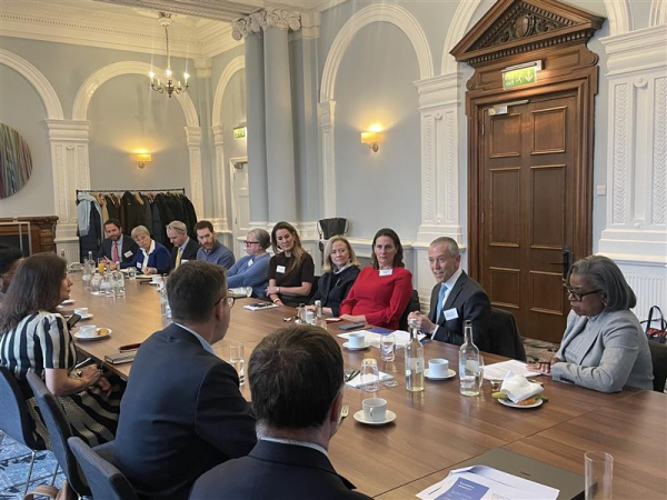 A group of professionals seated around a long wooden table in a formal conference room with high ceilings and arched walls.