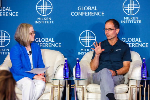 Two panelists having a discussion on stage at the Global Conference, seated in white chairs with blue branded backdrop