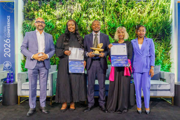 Five professionals holding certificates standing together outdoors under green foliage with blue banners