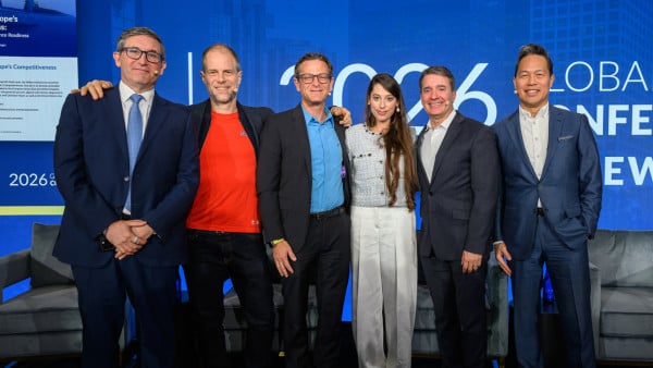 Group of seven business professionals posing together at a corporate event with blue backdrop