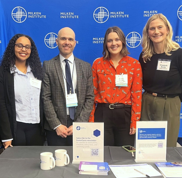 Four professionals standing behind a conference table with promotional materials and branded backdrop