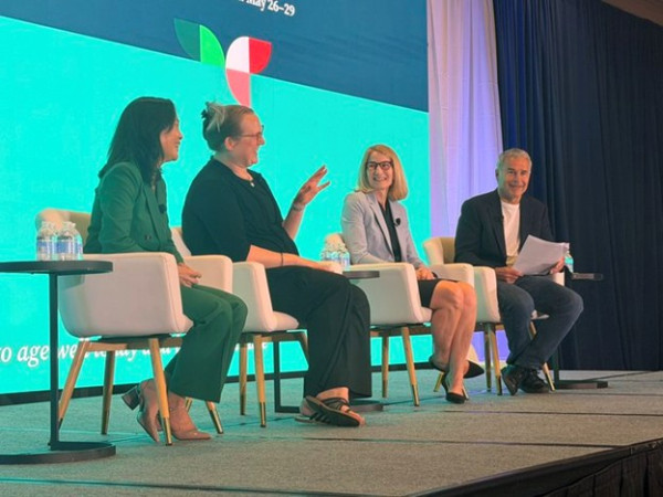 Four panelists seated on stage during a discussion with turquoise backdrop