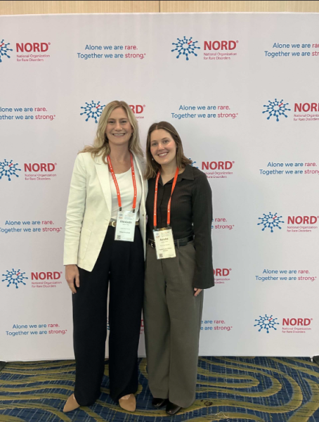 Two women standing together smiling at NOMO conference with branded backdrop