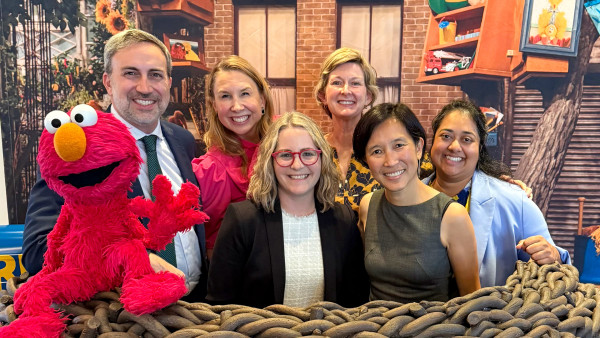 Group of seven people posing together indoors, including person in red Elmo costume