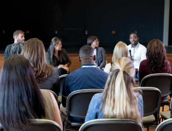 A group of people sit looking forward to watch a panel of speakers talk