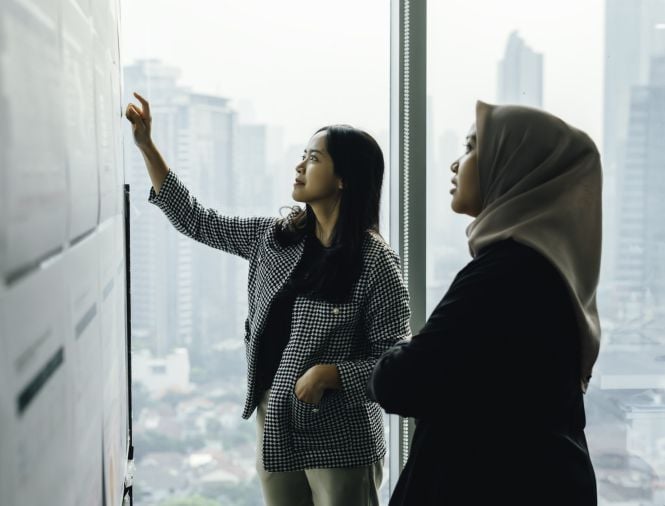 Two women in an office look at set of data on a wall