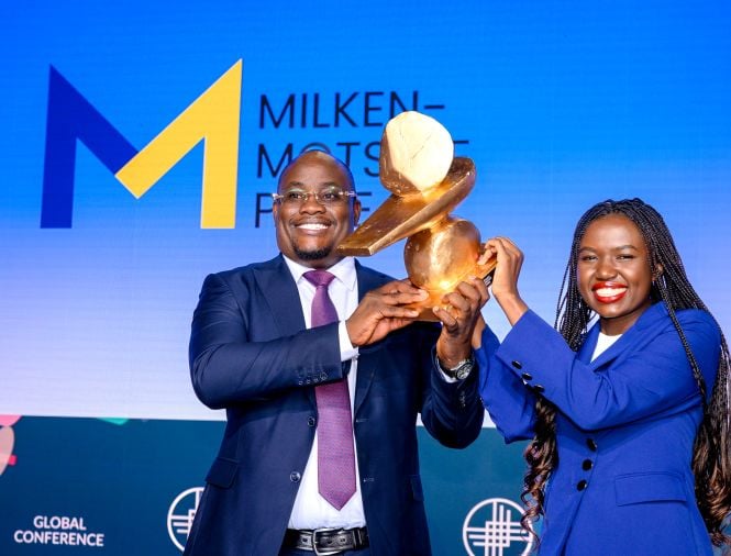 A Black man and Black woman receive an award for winning a competition while standing on a stage at a big event