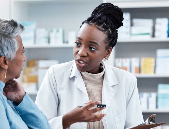 A young Black female pharmacist speaks with an older person