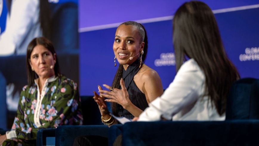 An image of speakers from The Milken Institute's Global Conference 2024 that is being used in preparation of Global Conference 2024. There are three women speakers, discussing a "Solving Challenges" panel. One woman has tanned white skin and short black hair, and she is looking at the middle speaker with a serious expression. The middle speaker is a woman with light brown skin and brown hair, and she is actively speaking. The third speaker has long black hair and is also facing the middle speaker.