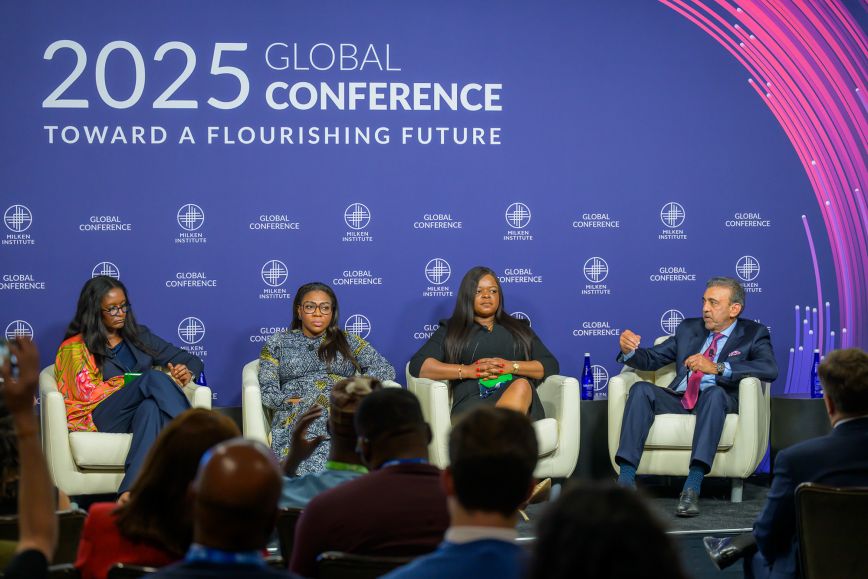 Four panelists seated on stage in front of a large “2025 Global Conference: Toward a Flourishing Future” backdrop, engaging in discussion while an audience looks on; participants include three women and one man in formal attire.