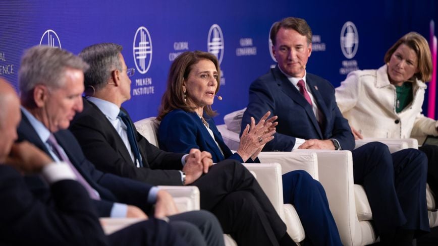 Panelists sit onstage at the Milken Institute Global Conference, engaged in a moderated discussion, with one speaker addressing the audience as others listen.