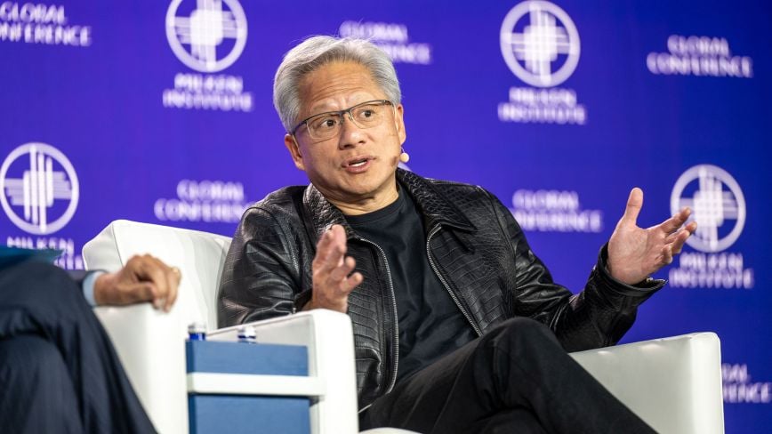 Panelist speaks while seated onstage at the Milken Institute Global Conference, gesturing during a discussion against a blue conference backdrop.