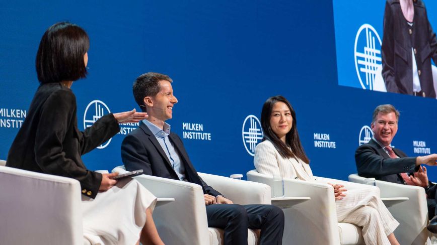 A diverse panel of four professionals engaging in a lively discussion on stage at a Milken Institute event.