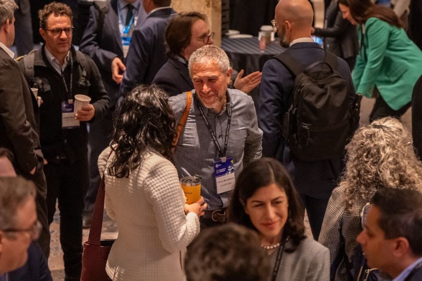 Two smiling attendees wearing event lanyards at the Milken Institute 2025 Finance Forum.
