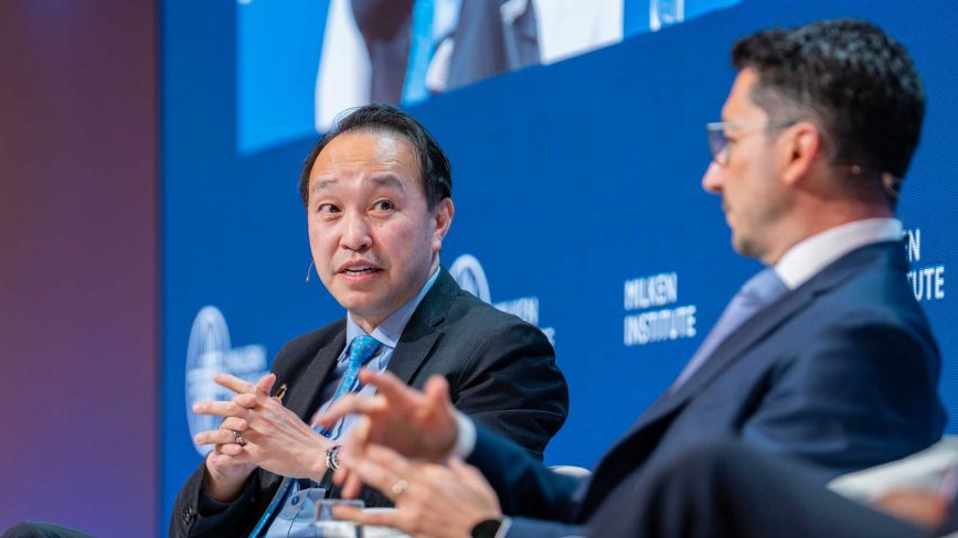 A close-up of a man in a dark suit and blue tie speaking expressively during a panel discussion.