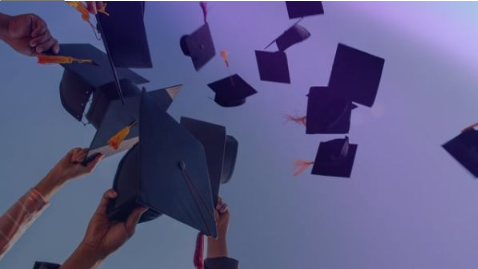 A group of graduates tossing their black mortarboard caps with orange tassels into the air against a gradient purple and blue sky.