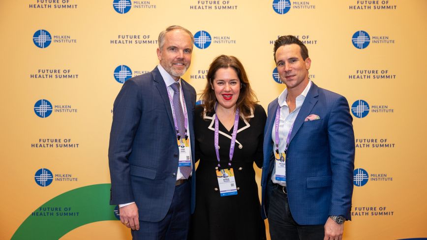 Three business professionals in formal attire posing together at a conference event with branded backdrop