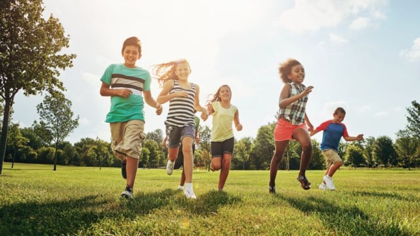 Five children running and playing together on a sunny grass field