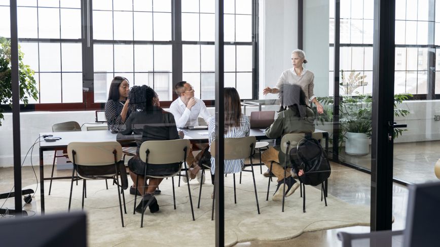 Modern office workspace with people working at tables near large industrial windows