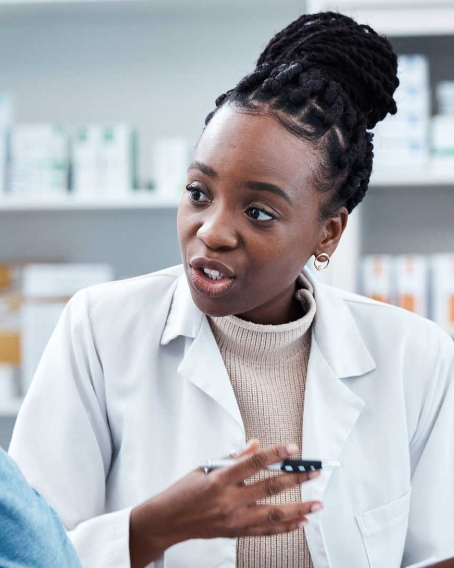 A young Black female pharmacist speaks with an older person