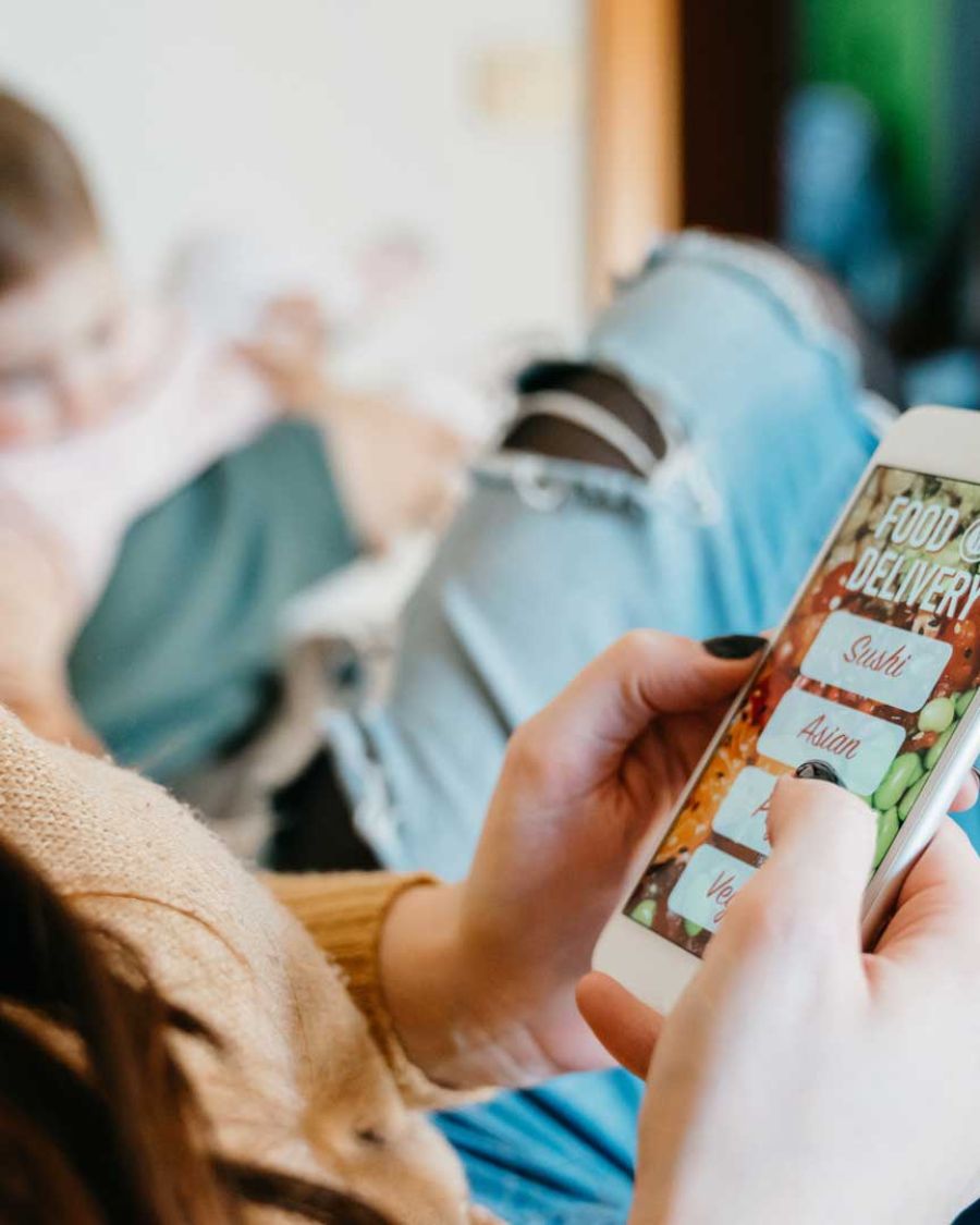 A woman sits with her phone in her hand making an order of groceries on an app