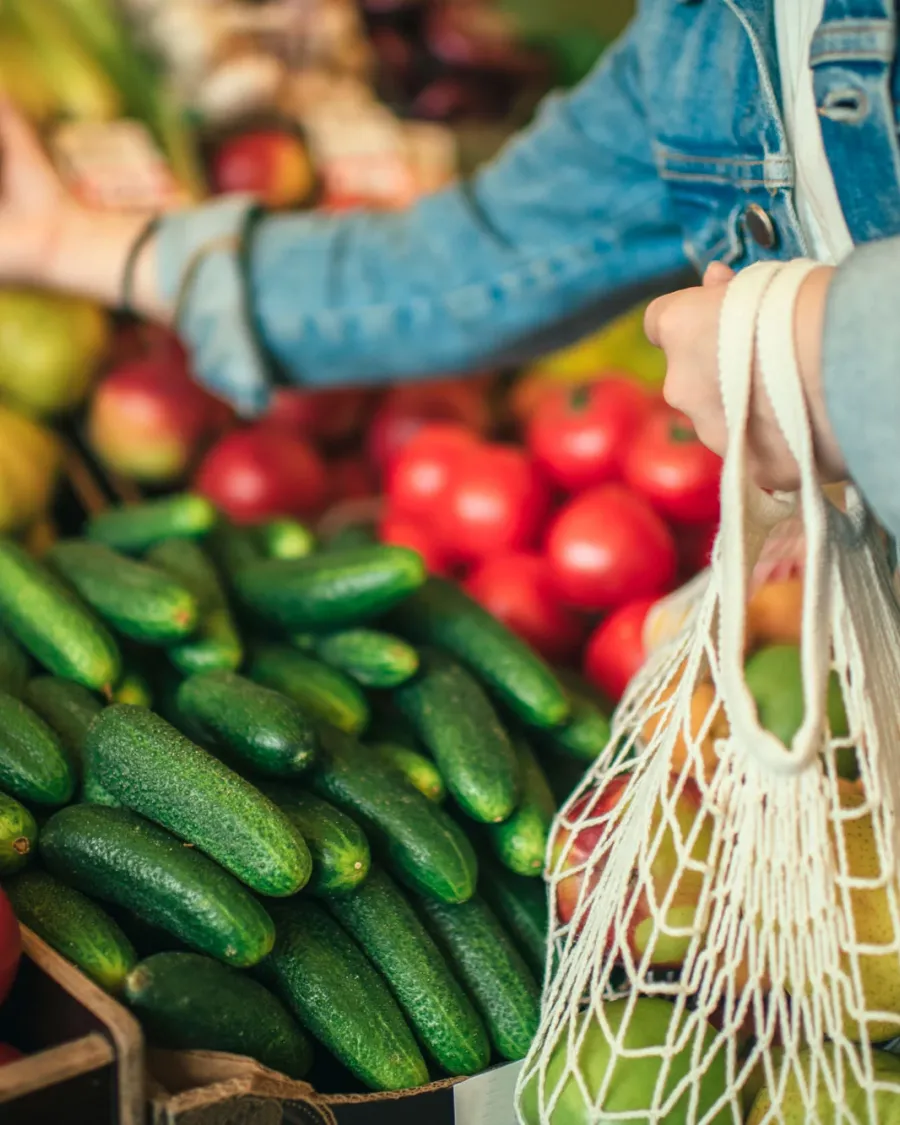 A woman shops with a mesh bag for fresh produce on stands