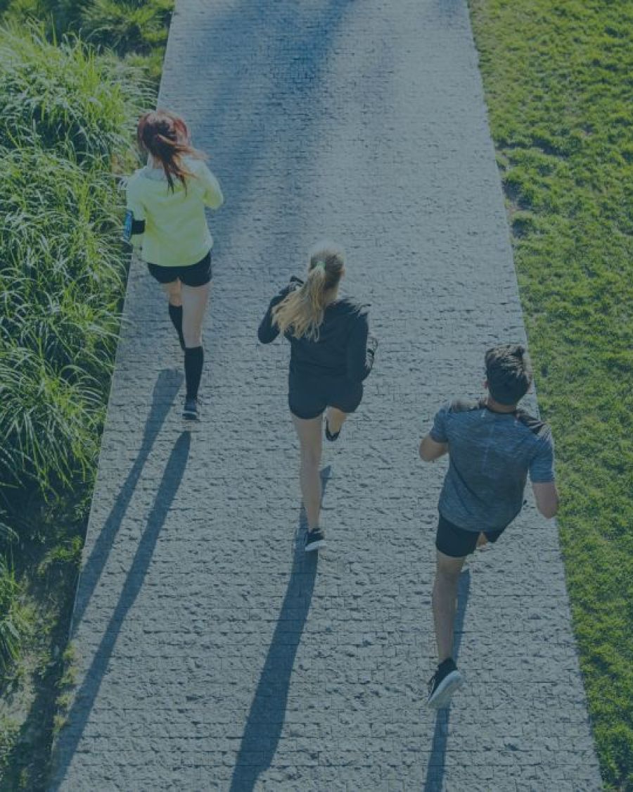 An aerial image with a blue-ish overlay of three people wearing workout attire and walking on a path.