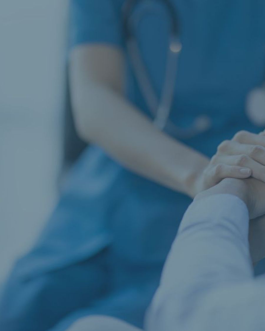 An image with a blue-ish overlay of a doctor's or nurse's hands holding a patient's hands.