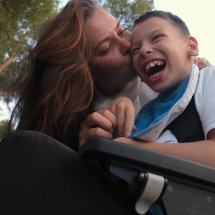 Young women gives a happy looking boy in a wheelchair a kiss on the cheek
