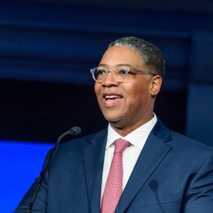 A Black man speaks at a podium on a stage