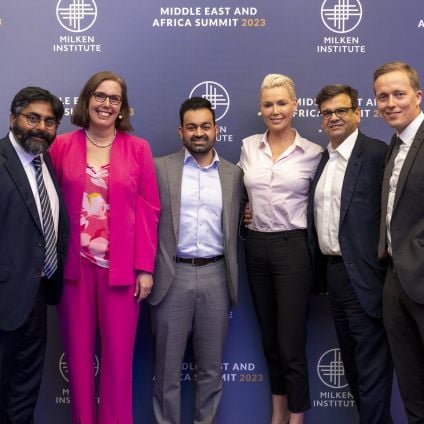 A group of six panelists post for a photo with a step and repeat in the background