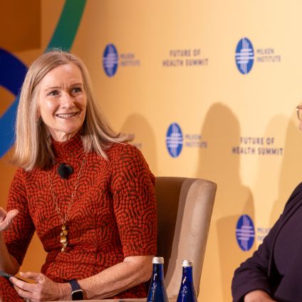 Three women in business attire conversing at an event with branded backdrop