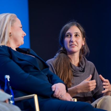 Two women in conversation at a panel discussion, one in navy blazer and one in olive top