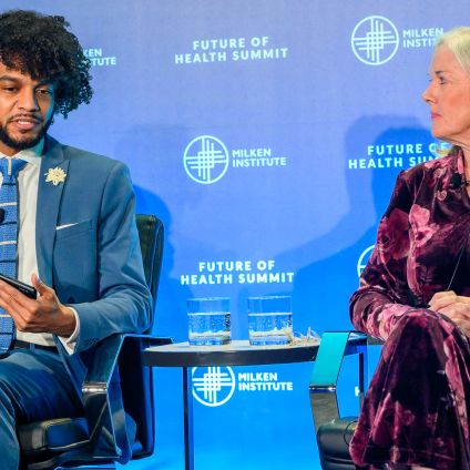 Panel discussion with two seated speakers, man in suit and woman in purple floral dress, with blue branded backdrop