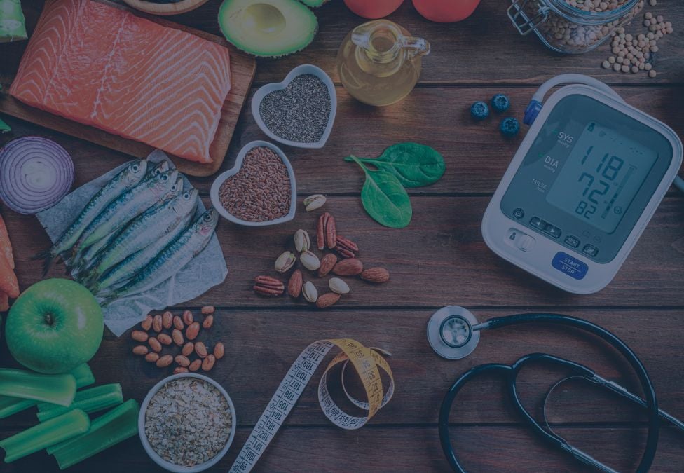 Fish, produce and a blood pressure monitor on a wooden surface