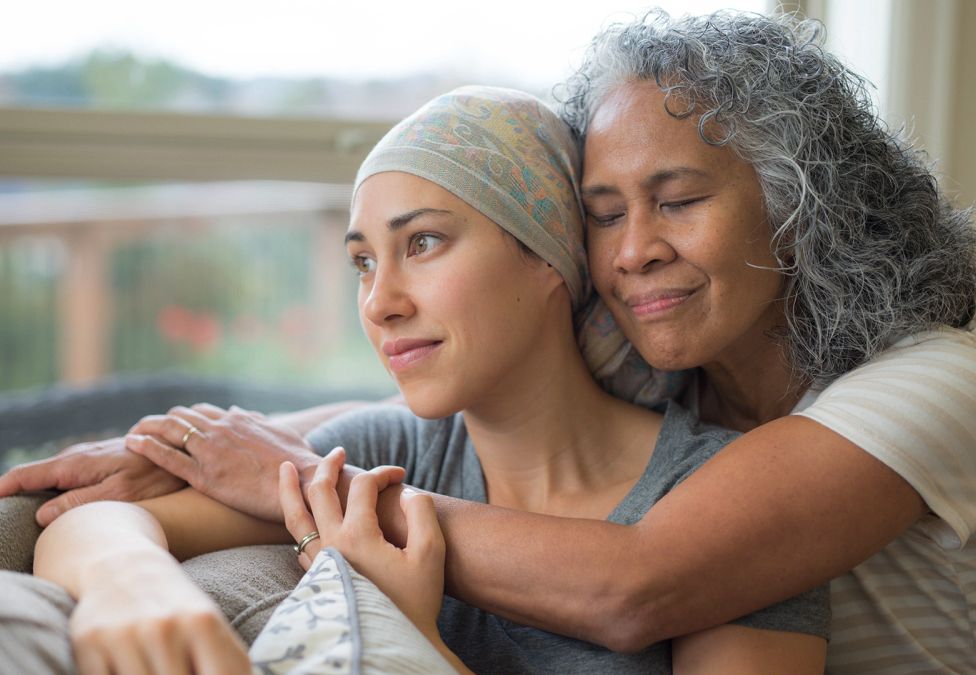 An older woman hugging a younger woman sitting against a couch