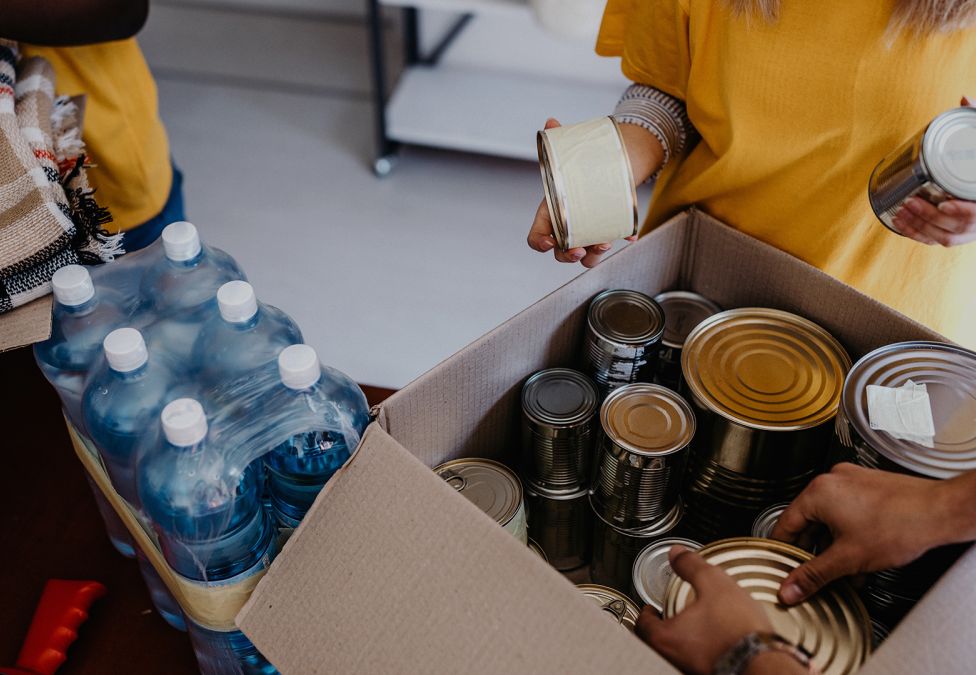 A person packs cans and supplies in a cardboard box