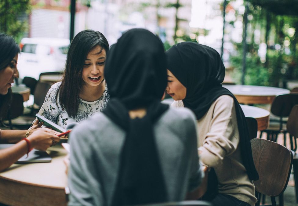 Four women sit around a table in conversation