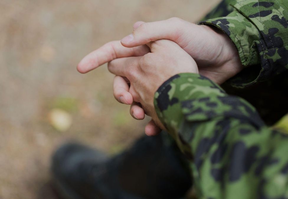 A person holding their hands wearing a green camo long-sleeved shirt