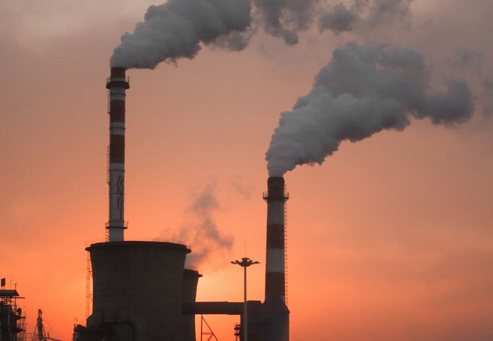 Two smoke stacks releasing smoke against a sunset sky