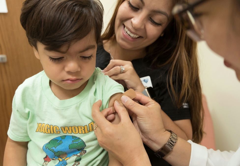 A child sitting on his mother's lap getting a bandaid from a doctor or nurse after a shot