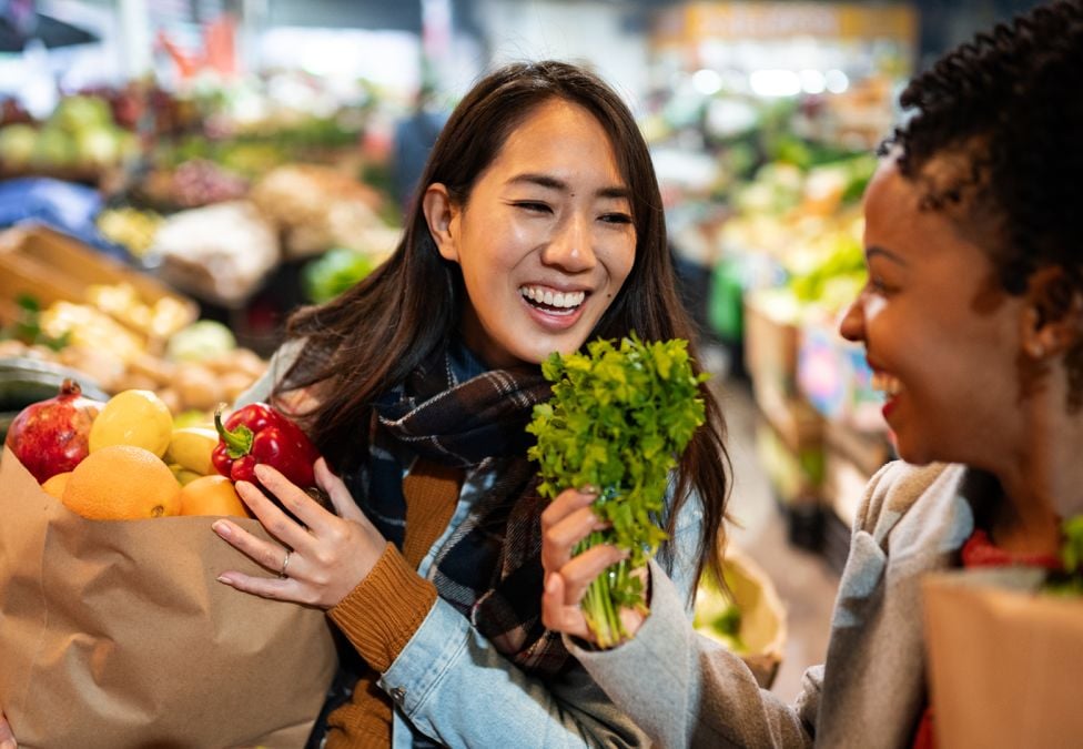 Two smiling women shop for groceries in the produce section