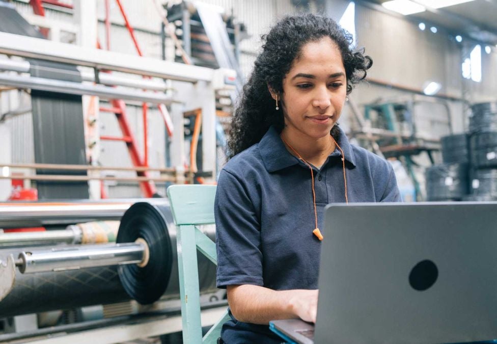 A female worker standing at a desk with a computer in a manufacturing setting