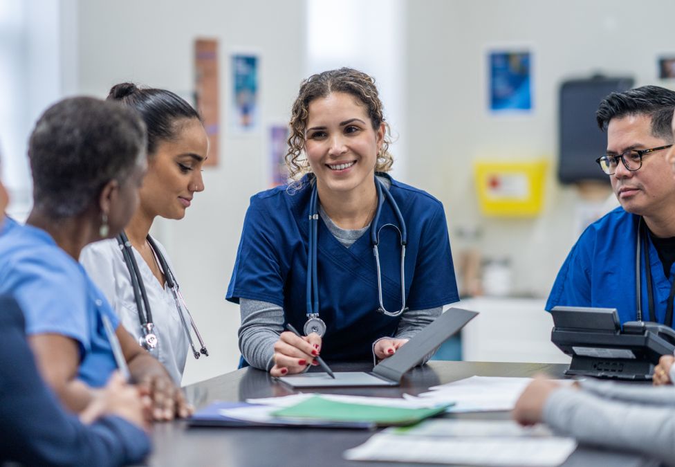A doctor speaks to other health care workers at a table.