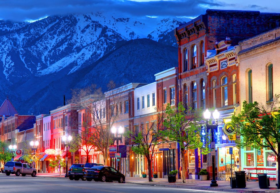 The Rise of Mid-Sized American Cities: The Drivers of Perfectly-Sized Growth A city street with low-rise connected buildings lining the street and a snowy mountain background, leading to an article titled "The Rise of Mid-Sized American Cities: The Drivers of Perfectly-Sized Growth"